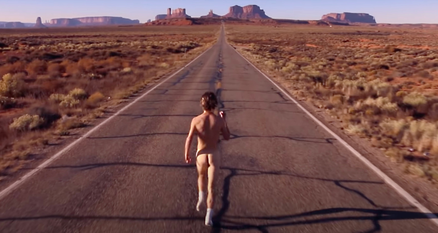 One skinny naked white dude running down a desert highway.